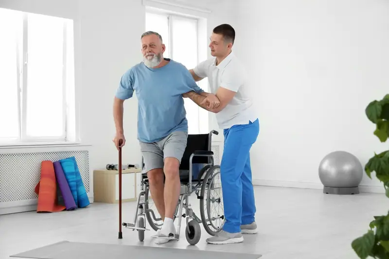 Therapist helping an older man rise from a wheelchair with a cane